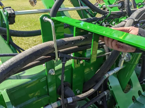 A person is holding a Mounting Bracket Kit for John Deere 1790/95 Planters with Interplant on a tractor.