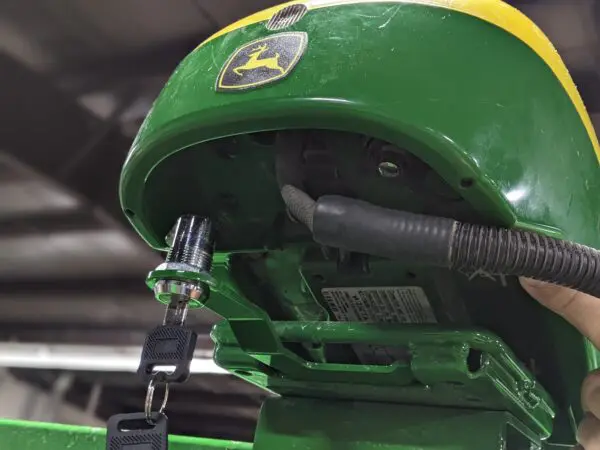 A person is holding a green GPS Globe Lock for John Deere® 6000 series StarFire tractor.