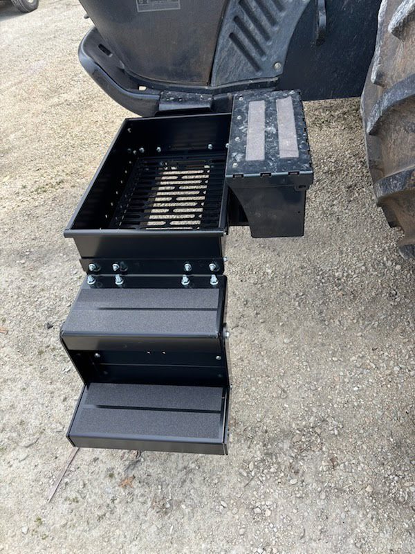 Tractor steps and toolbox on dirt ground.