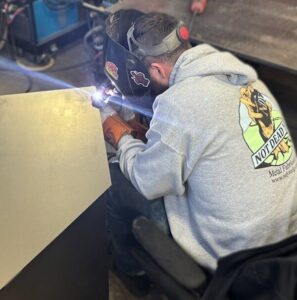 a welder in a grey sweater welding a sheet of metal